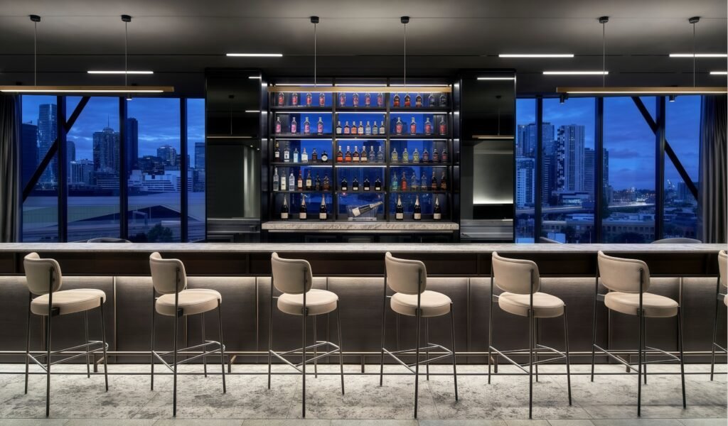 Hotel bar interior with neatly arranged bar stools and a custom back bar wall showcasing a variety of liquors.