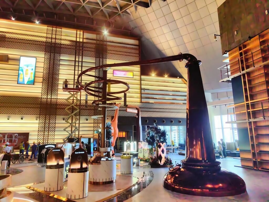 Workers assembling a massive display system in a whisky museum, surrounded by floor-to-ceiling wall-mounted whisky cabinets.